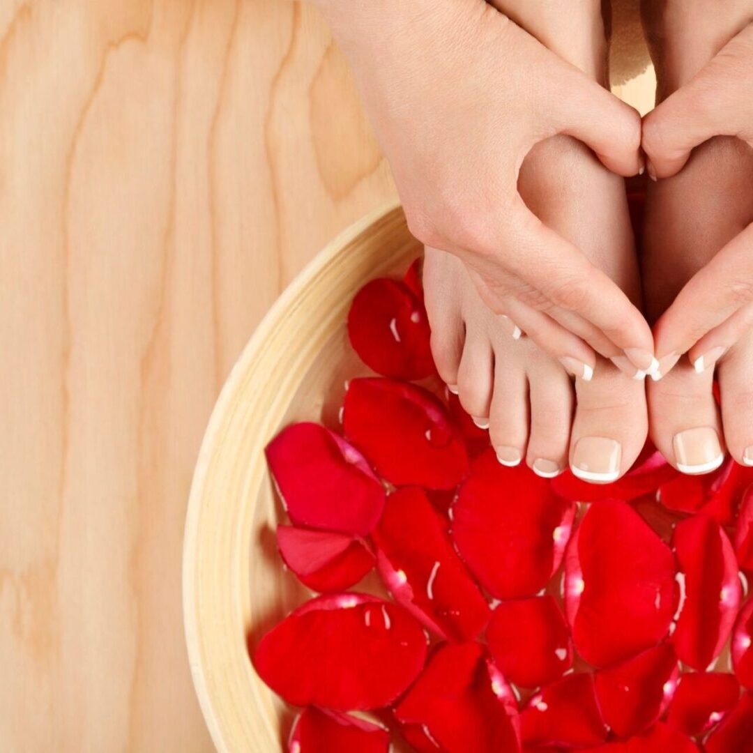 A person is getting their feet washed in a bowl of red petals.